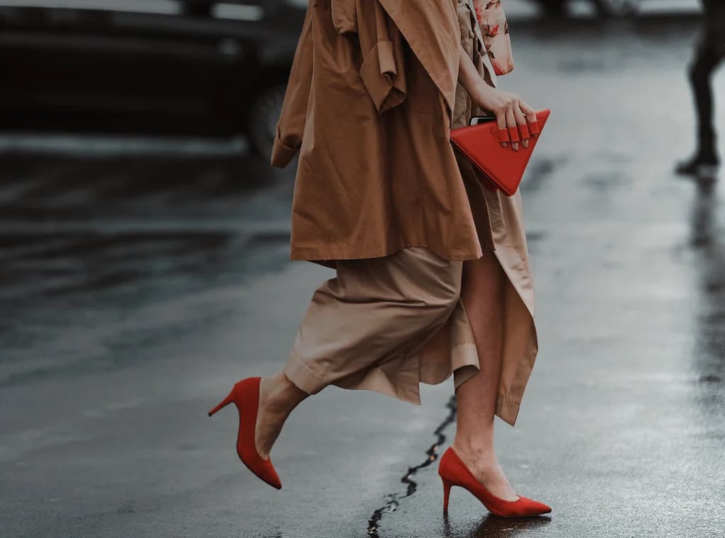 Una mujer bien vestida, con hermosos tacones altos rojos y un bolso rojo de moda, cruza la calle. Se superpone la frase francesa "bien habillé" con su traducción al español, "bien vestido".